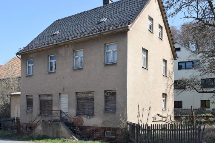 Altes, zweistöckiges Haus mit verfallener Fassade und geschlossenen Fensterläden.
