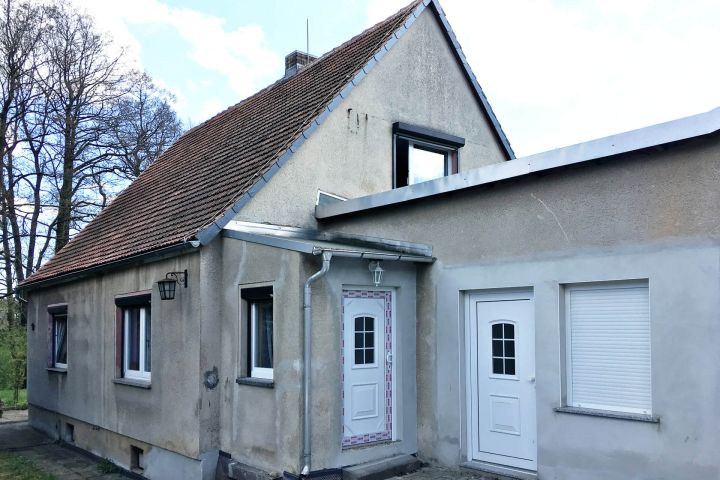 Ein einfaches Haus mit Satteldach, zwei Türen und mehreren Fenstern.